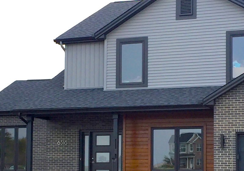two story ranch with dark grey siding, black trim, real cedar siding, black garage door, dark brown brick